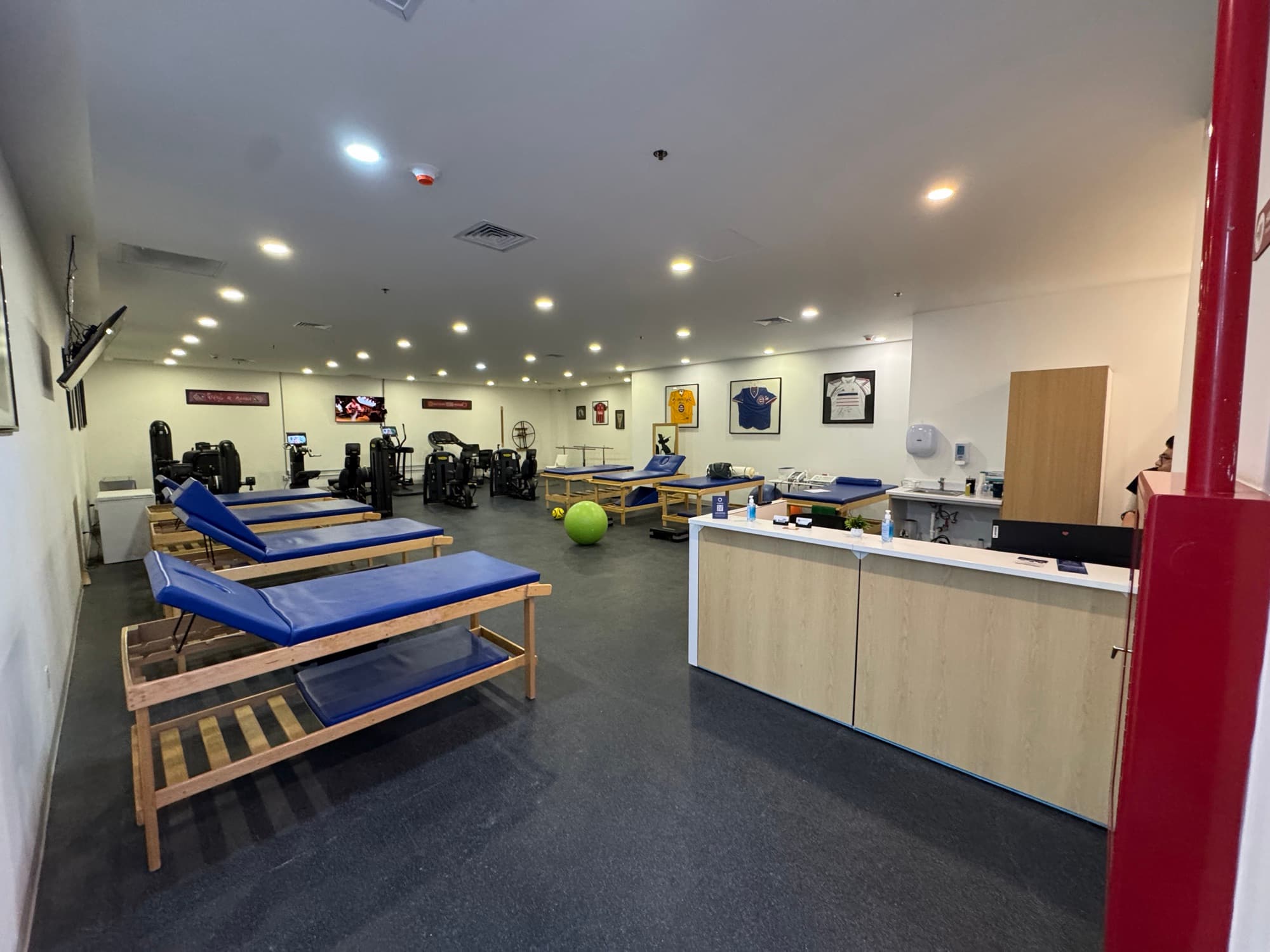 Gimnasio de rehabilitación física con camillas acolchadas, equipo de ejercicio y un mostrador de recepción
