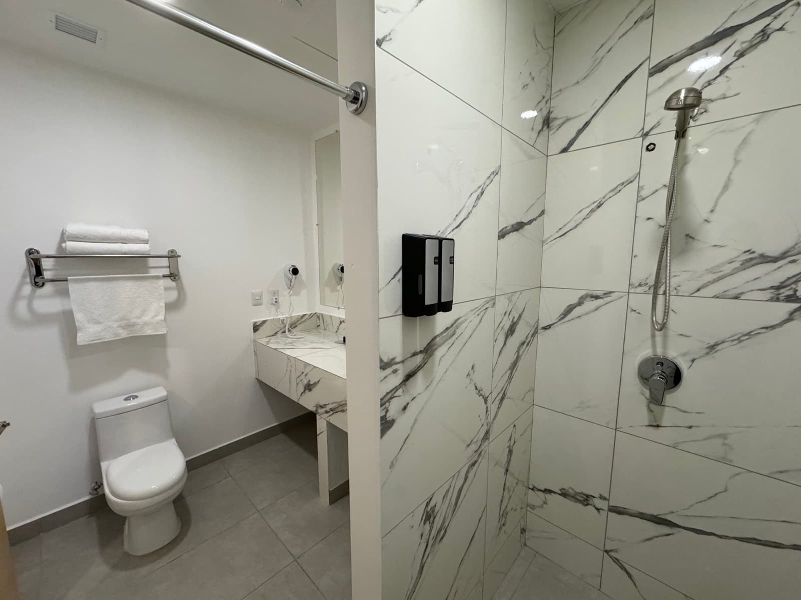 Baño privado con regadera de mármol sin puerta, inodoro, lavabo y toallas dobladas en un toallero