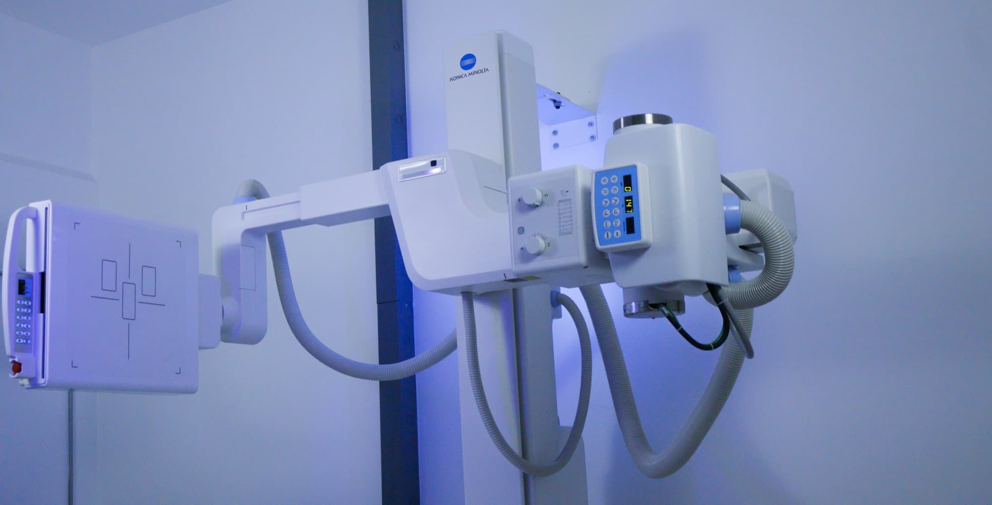 Cabezal de rayos X sobre un brazo suspendido frente a un detector montado en la pared