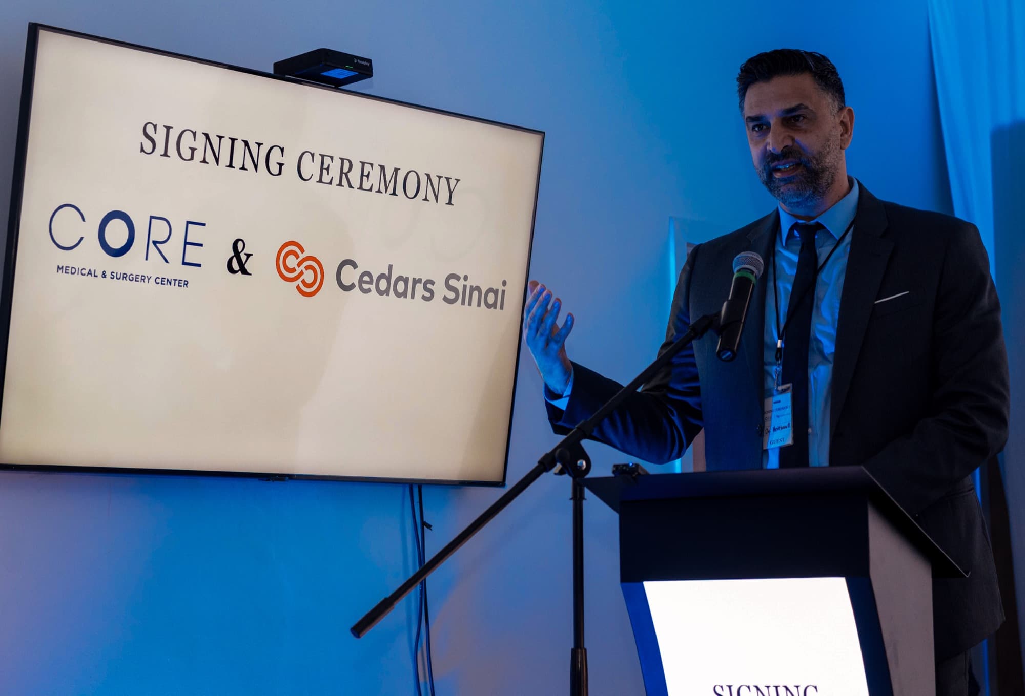 A man in a suit speaks into a podium microphone beside a screen reading Signing Ceremony